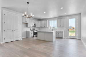 Kitchen featuring a chandelier, light wood-type flooring, gray cabinets, stainless steel appliances, and hanging light fixtures