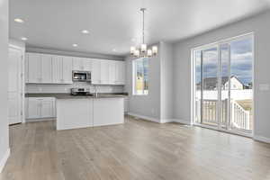 Kitchen featuring range, pendant lighting, light wood-type flooring, an island with sink, and white cabinetry