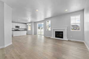 Unfurnished living room with a textured ceiling, light hardwood / wood-style flooring, and a notable chandelier