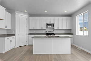 Kitchen with range, white cabinetry, light hardwood / wood-style floors, and an island with sink