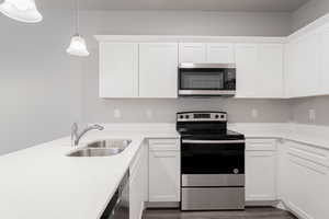 Kitchen with white cabinetry, appliances with stainless steel finishes, sink, and decorative light fixtures