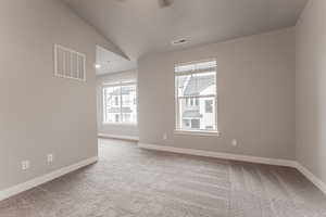 Spare room featuring lofted ceiling, light colored carpet, and a wealth of natural light