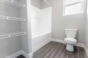 Bathroom with toilet, bathtub / shower combination, and wood-type flooring