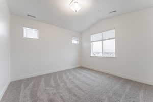 Spare room featuring carpet, a healthy amount of sunlight, and vaulted ceiling