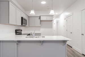 Kitchen with range with electric stovetop, a breakfast bar area, hanging light fixtures, sink, and light wood-type flooring