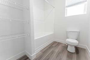 Bathroom with toilet, shower / bath combination, and hardwood / wood-style floors