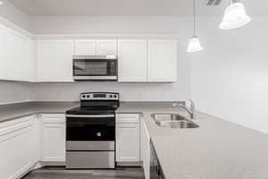 Kitchen featuring sink, stainless steel appliances, pendant lighting, white cabinets, and dark hardwood / wood-style floors