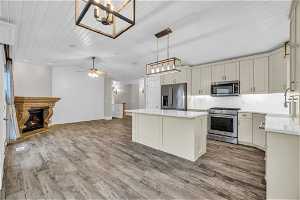 Kitchen featuring wood-type flooring, backsplash, ceiling fan with notable chandelier, and stainless steel appliances