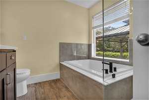 Bathroom featuring wood-type flooring, vanity, toilet, and tiled bath