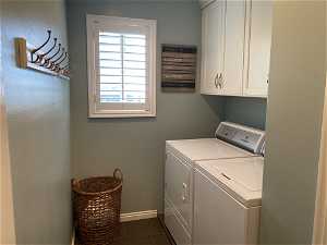 Clothes washing area featuring dark tile flooring, cabinets, and washer and dryer