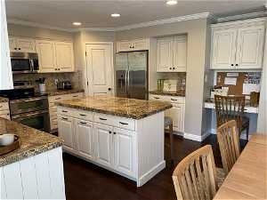 Kitchen featuring appliances with stainless steel finishes, a kitchen island, tasteful backsplash, white cabinets, and dark hardwood / wood-style flooring