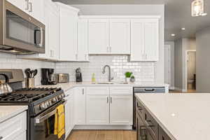 Kitchen with white cabinets, light hardwood / wood-style flooring, backsplash, appliances with stainless steel finishes, and sink