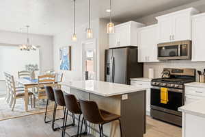 Kitchen with appliances with stainless steel finishes, a kitchen island, tasteful backsplash, white cabinetry, and hanging light fixtures