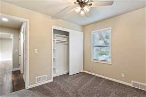 Unfurnished bedroom featuring a closet, ceiling fan, and dark carpet
