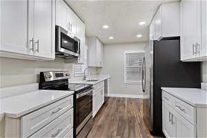 Kitchen with sink, white cabinetry, stainless steel appliances, and dark wood-type flooring