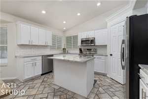 Kitchen with a center island, white cabinets, backsplash, lofted ceiling, and stainless steel appliances