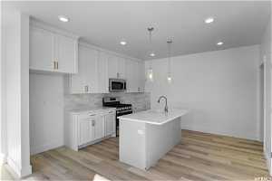 Kitchen with hanging light fixtures, light hardwood / wood-style flooring, white cabinetry, backsplash, and appliances with stainless steel finishes