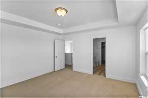 Unfurnished bedroom with a raised ceiling, ensuite bathroom, and carpet floors