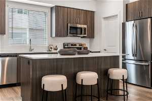 Kitchen with a kitchen island, stainless steel appliances, dark brown cabinetry, and light wood-type flooring