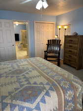 Bedroom with a textured ceiling, ceiling fan, connected bathroom, and carpet flooring