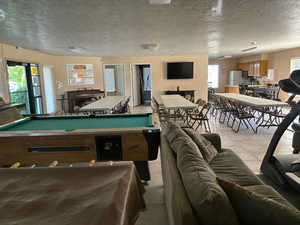 Rec room featuring a textured ceiling, a fireplace, pool table, and light tile flooring