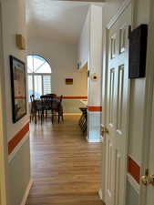 Corridor featuring lofted ceiling, light hardwood / wood-style floors, and a textured ceiling