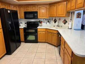 Kitchen featuring kitchen peninsula, black appliances, sink, and light tile flooring