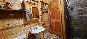 Bathroom with tile flooring, wooden walls, and toilet
