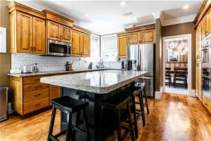 Kitchen with a center island, light hardwood / wood-style floors, black appliances, and a breakfast bar
