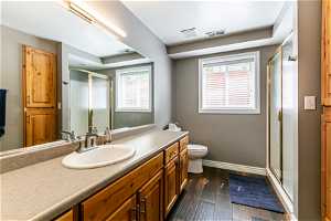 Bathroom with hardwood / wood-style floors, a shower with shower door, toilet, and vanity with extensive cabinet space