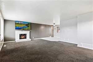 Unfurnished living room featuring ceiling fan, dark carpet, and a fireplace