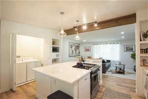 Kitchen featuring independent washer and dryer, appliances with stainless steel finishes, light wood-type flooring, and a kitchen island