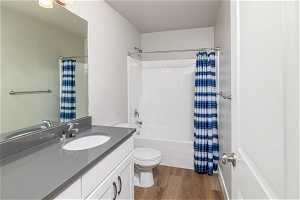 Full bathroom with wood-type flooring, oversized vanity, shower / bath combination with curtain, and toilet