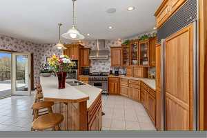 Kitchen with wall chimney exhaust hood, high end appliances, light tile floors, and an island with sink