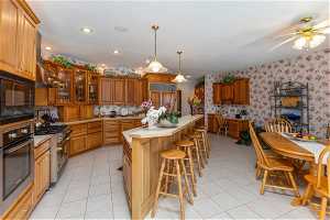 Kitchen with a center island, built in appliances, ceiling fan, and light tile flooring