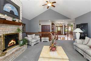 Living room featuring high vaulted ceiling, ceiling fan, a brick fireplace, and carpet floors