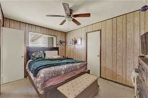 Bedroom featuring light colored carpet, ceiling fan, and wood walls