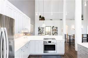 Kitchen with appliances with stainless steel finishes, white cabinets, dark wood-type flooring, a high ceiling, and kitchen peninsula