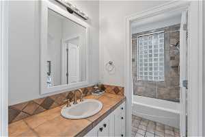 Secondary primary bathroom featuring tiled shower / bath combo, tasteful backsplash, vanity, and tile floors