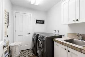 Clothes washing area featuring separate washer and dryer, tile flooring, cabinets, and sink