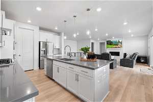 Kitchen featuring stainless steel appliances, an island with sink, white cabinets, sink, and light wood-type flooring
