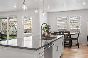 Kitchen featuring hanging light fixtures, a center island with sink, light hardwood / wood-style floors, white cabinets, and stainless steel dishwasher