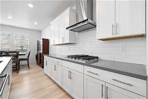 Kitchen with wall chimney exhaust hood, white cabinets, light hardwood / wood-style floors, backsplash, and gas stovetop