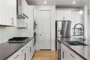 Kitchen featuring white cabinets, light hardwood / wood-style flooring, backsplash, appliances with stainless steel finishes, and wall chimney range hood