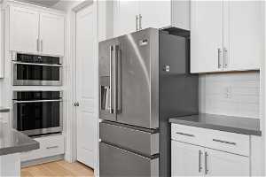 Kitchen with appliances with stainless steel finishes, backsplash, light wood-type flooring, and white cabinetry
