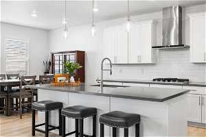 Kitchen featuring stainless steel gas stovetop, light hardwood / wood-style floors, wall chimney range hood, tasteful backsplash, and hanging light fixtures