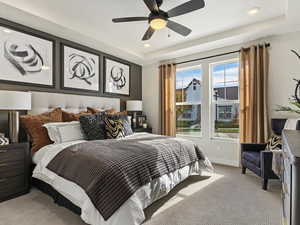 Bedroom with ceiling fan, a tray ceiling, and carpet flooring