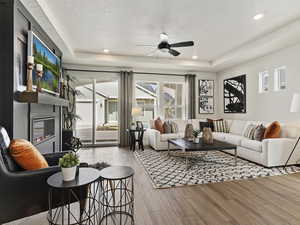 Living room featuring ceiling fan, light wood-type flooring, a tray ceiling, and a textured ceiling