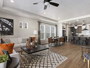 Living room with a wealth of natural light, a raised ceiling, ceiling fan, and hardwood / wood-style flooring