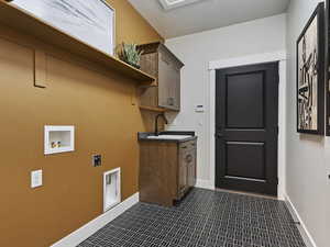 Clothes washing area with dark tile floors, cabinets, sink, electric dryer hookup, and washer hookup